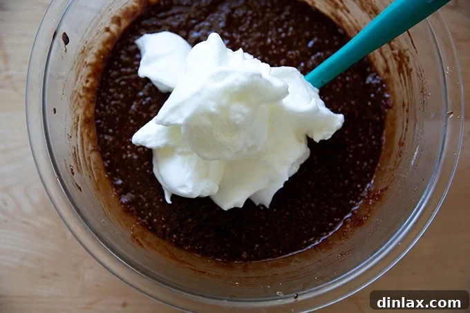 Classic Caprese Flourless Chocolate Almond Torte 11 The initial stage of gently folding beaten egg whites into the dark Torta Caprese batter, showing soft, white streaks merging.