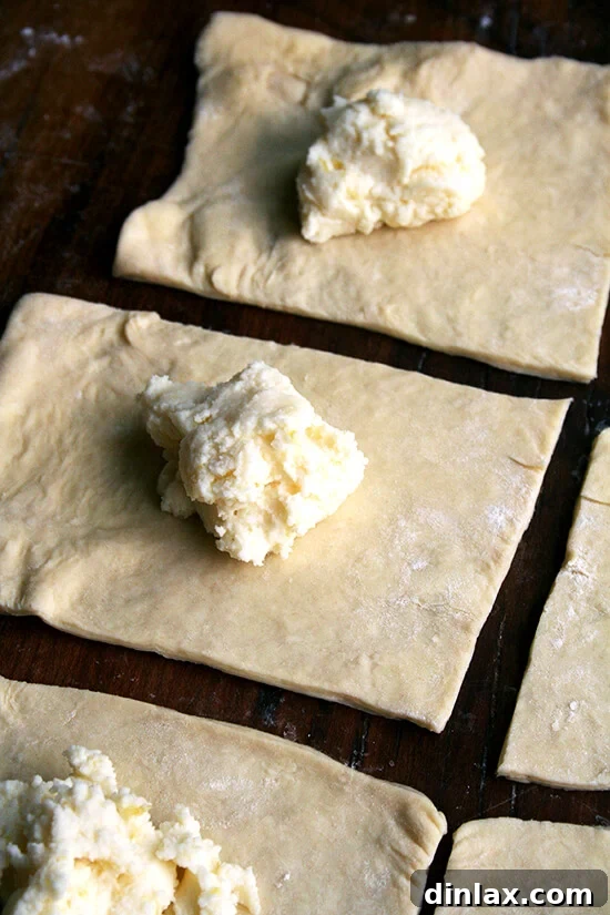 Danish pastry dough cut into 8 squares, each topped with a tablespoon of the creamy ricotta filling, poised for shaping.