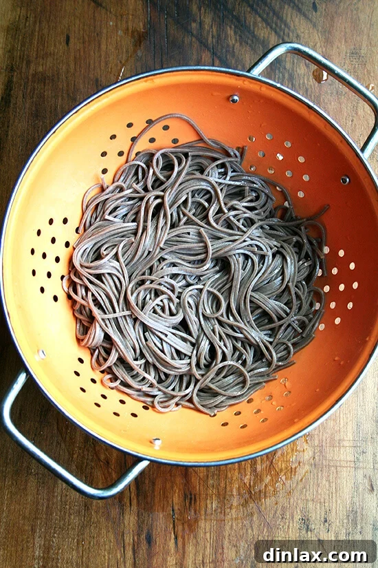 Cooked soba noodles draining in a colander under cold water