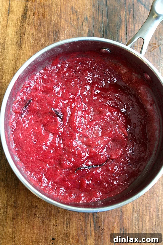 Jammy Rhubarb Ripple Ice Cream 8 Cooked rhubarb jam simmering in a saucepan, now thickened and vibrant in color, with visible vanilla bean flecks, almost ready.