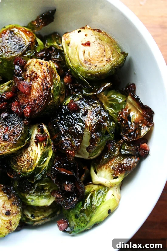 Overhead close-up of beautifully roasted Brussels sprouts with olive oil, salt, pepper, and crispy pancetta, served in a pristine white bowl. The sprouts are glistening and caramelized.