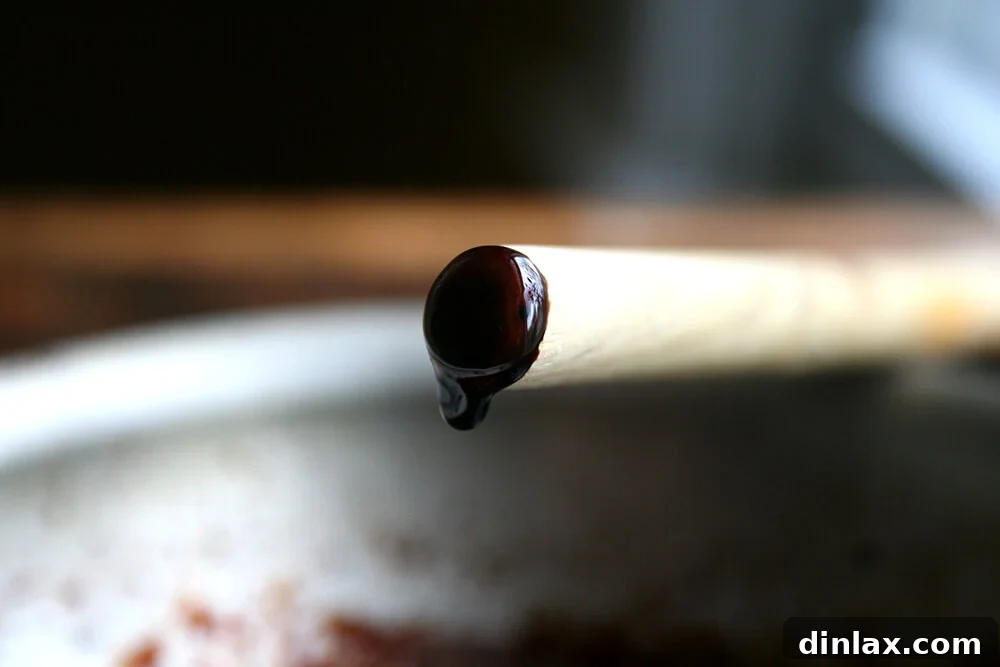 Close-up shot of thick, syrupy balsamic reduction slowly dripping off the end of a wooden spoon, showcasing its perfect consistency.