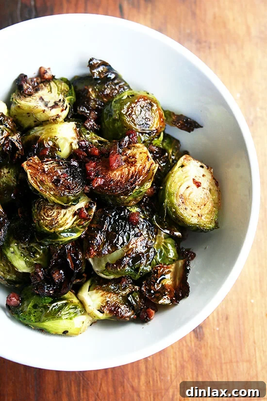 Close-up overhead view of perfectly roasted Brussels sprouts with olive oil, salt, pepper, and crispy pancetta, glistening in a small white serving bowl.