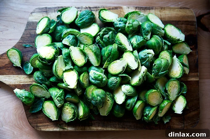 Neatly halved Brussels sprouts spread out on a wooden cutting board, showcasing their vibrant green interior.