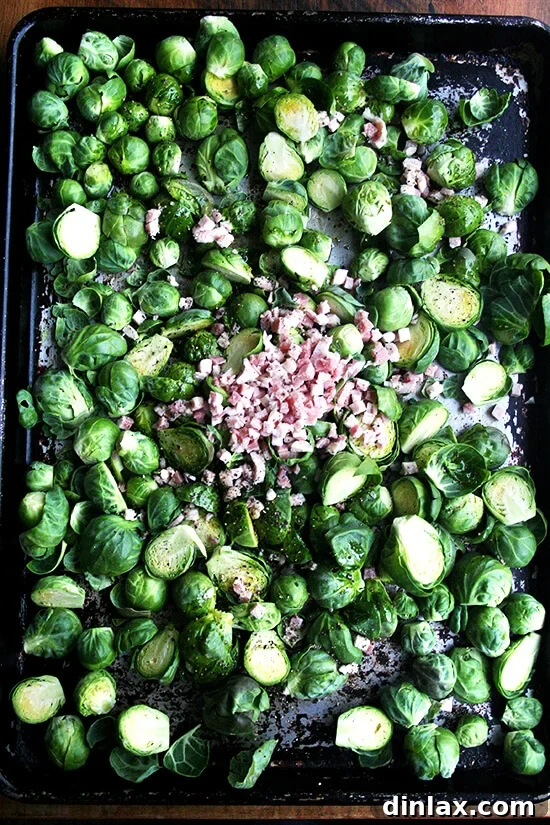 Brussels sprouts and diced pancetta spread evenly on a sheet pan, seasoned and ready to be roasted together.