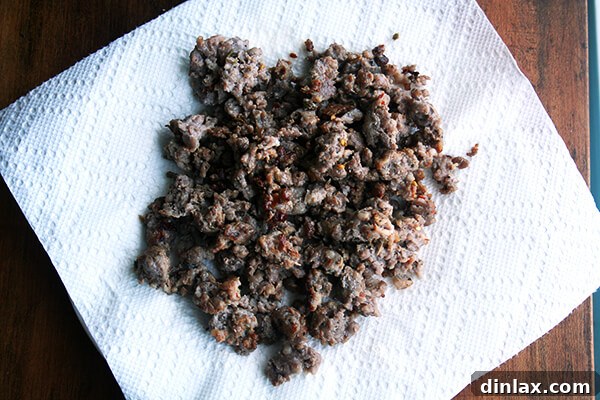 Hearty Italian Sausage, Escarole, and White Bean Soup 14 Cooked and browned sausage crumbles resting on a paper towel-lined plate, draining excess fat.