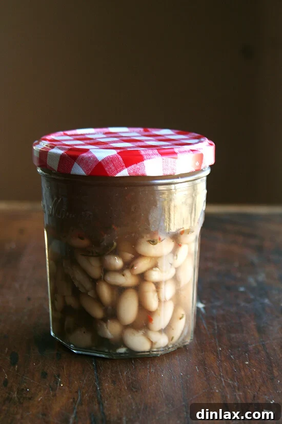 Cooked white beans, preserved in their flavorful cooking liquid, stored in a clear container.