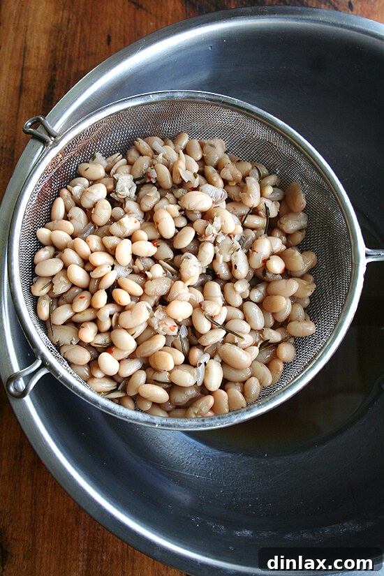 Hearty Italian Sausage, Escarole, and White Bean Soup 4 A metal strainer holding a generous quantity of perfectly cooked white beans, still glistening with their cooking liquid.