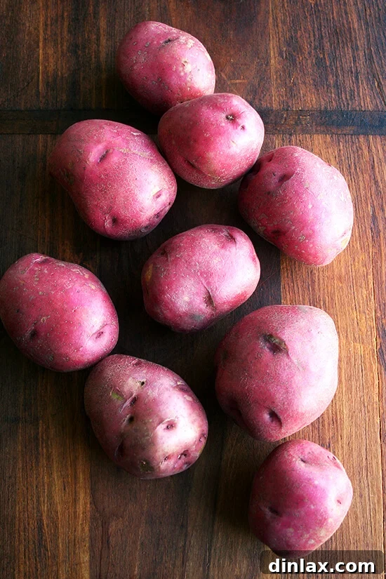 Alice Waters Perfected Potato Gratin 4 A pile of fresh red potatoes resting on a wooden cutting board, ready for peeling and slicing.