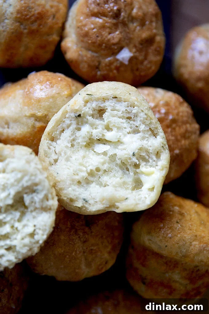 A close-up of a halved and buttered thyme dinner roll, revealing its perfectly airy texture.