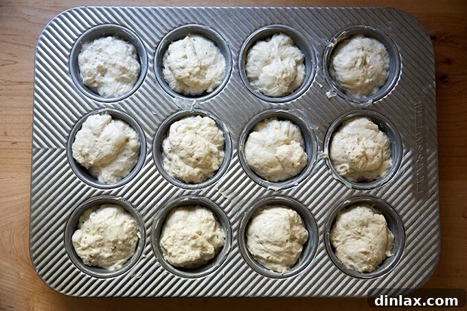 A muffin tin filled with unbaked dinner roll dough portions, ready for the second rise.