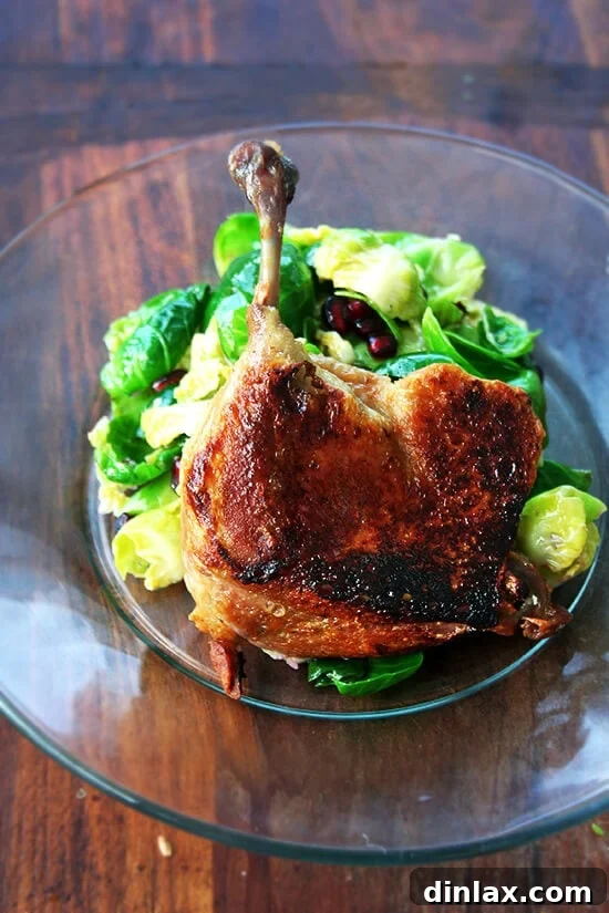 A perfectly cooked duck leg confit, golden and crispy, standing elegantly on a plate supported by a mound of fresh salad greens.