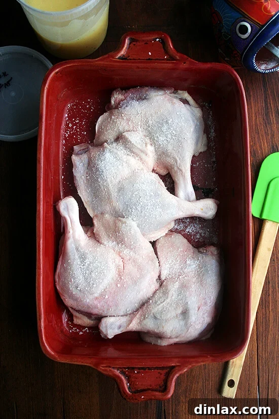 A baking dish with four raw duck legs, seasoned with salt, ready to be covered with stored, reusable duck fat for a subsequent batch of confit, showcasing the sustainable aspect of the recipe.