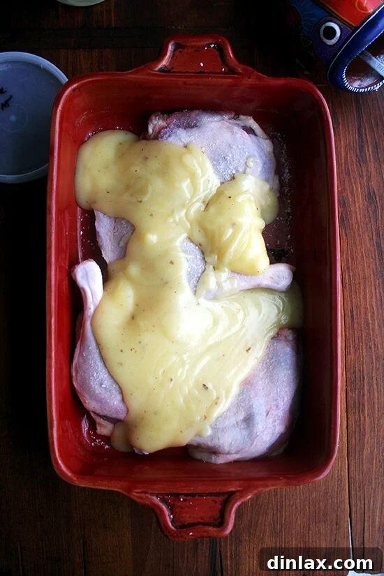 Four duck legs in a baking dish, seasoned and perfectly submerged in beautifully rendered, solidified duck fat, showcasing the preparation for a new confit batch.