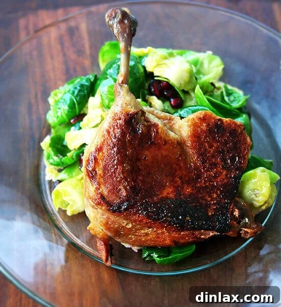A duck leg confit standing up on a plate supported by a mound of salad greens.