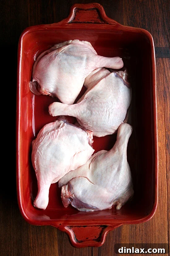 Four raw duck legs placed snugly in a red 9x13-inch baking dish, ready for seasoning.
