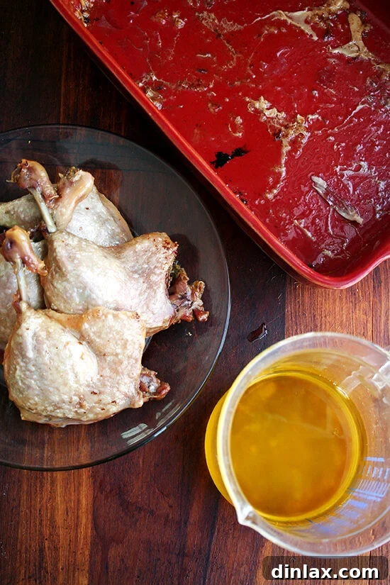 Four tender duck leg confits resting on a plate, with a liquid measuring cup filled with approximately 1.75 cups of retrieved rendered fat and butter.