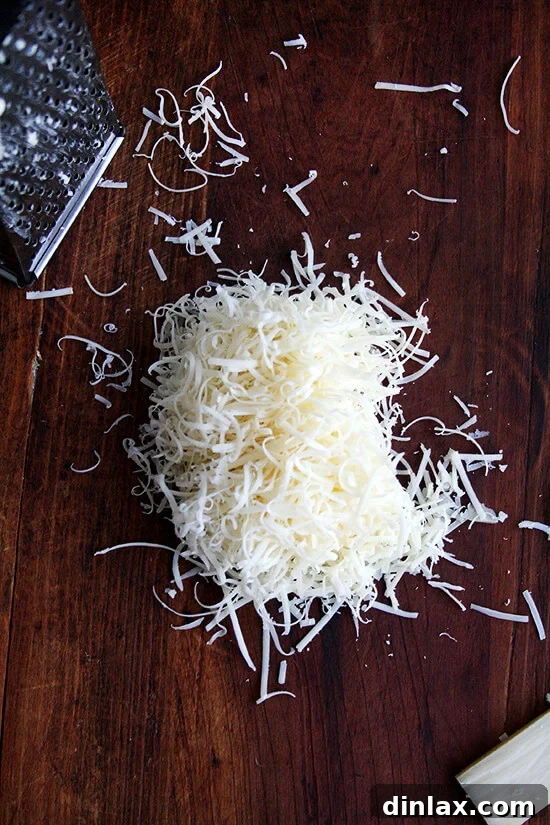 Freshly grated Gruyère cheese piled on a wooden board, ready for use.