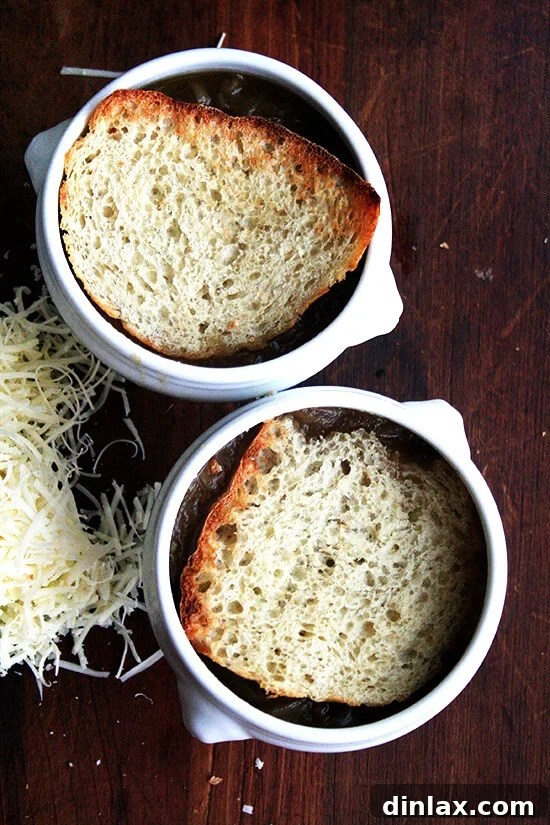 Two bowls of French Onion soup, topped with toasted bread, awaiting cheese for broiling.