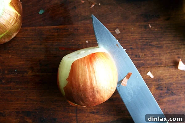 An onion on a cutting board with a knife making an initial score.