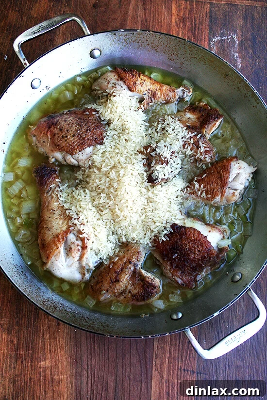 The Iconic Canal House Chicken and Rice 6 Rice being gently patted down among the chicken pieces in the pot, ready to absorb the flavorful braising liquid and cook into a comforting dish.