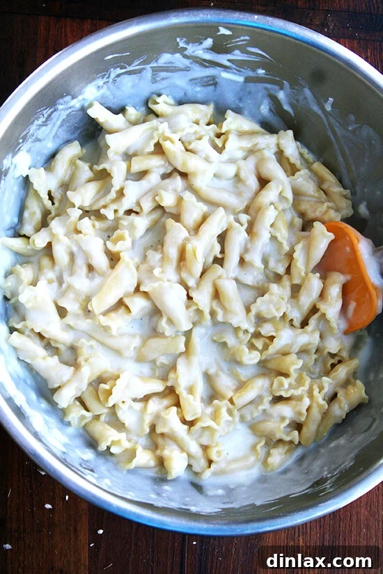 Parboiled pasta being tossed with béchamel sauce in a large mixing bowl.