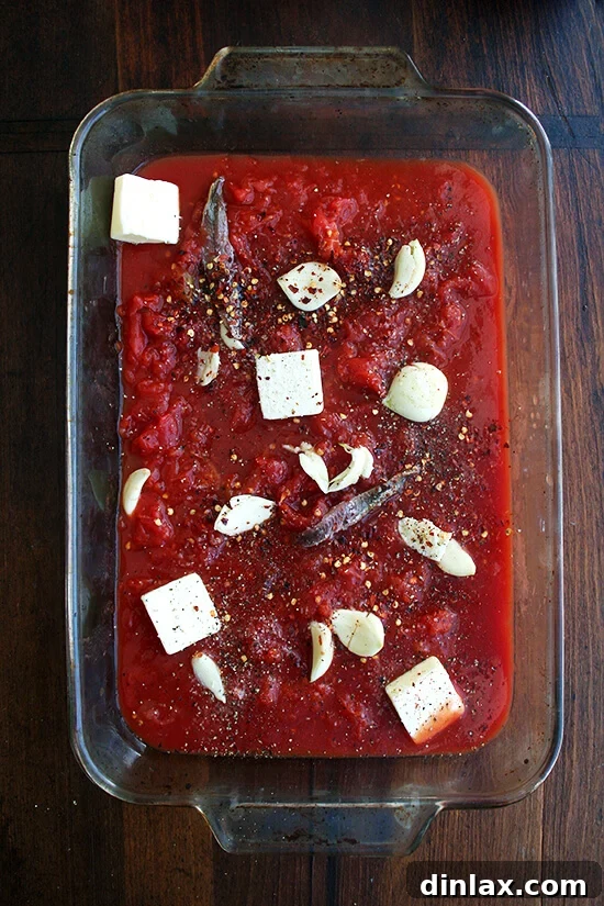 A selection of raw ingredients including canned tomatoes, garlic, anchovies, and butter, prepared for roasting.