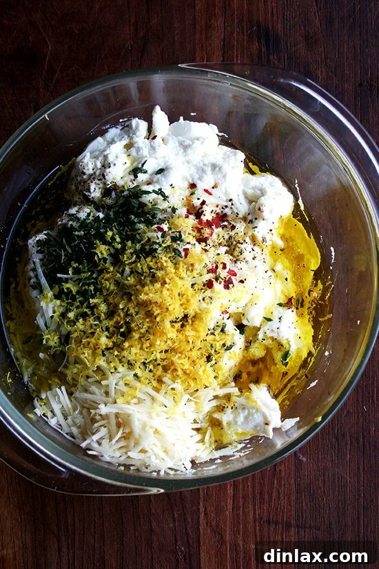 All the fresh ingredients for a batch of homemade baked ricotta, including a tub of ricotta, lemon, fresh thyme, garlic, olive oil, and parmesan cheese.