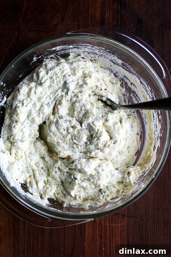 A bowl of ricotta mixed with lemon zest, minced garlic, fresh thyme, and seasonings, ready to be transferred to a baking dish.