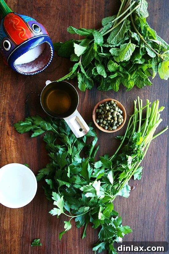 Fresh ingredients laid out for Nigella Lawson's mint sauce, including vibrant mint, parsley, capers, and cornichons.