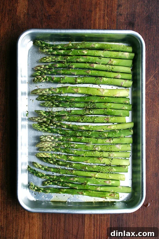 Fresh green asparagus spears seasoned and arranged neatly on a quarter sheet pan, ready for roasting.