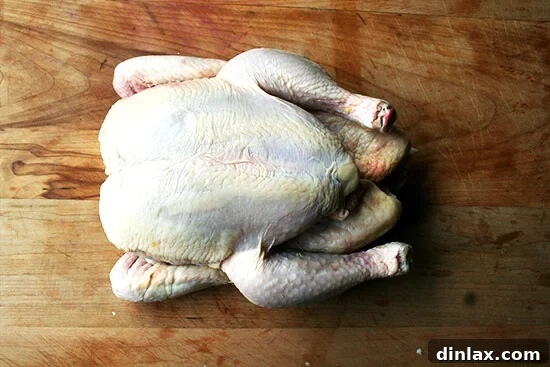 A whole, raw chicken resting on a clean cutting board, ready for butchering and preparation.