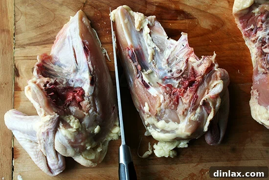 A raw chicken breast being carefully split in half with a knife, creating two separate portions for roasting.