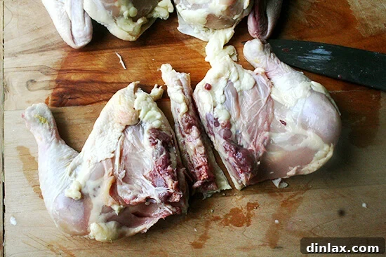 A knife cutting to separate the leg quarter (thigh and drumstick) from the breast portion of a raw chicken.