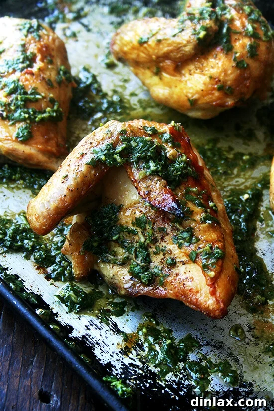 A close-up of the sheet pan showing golden-brown crispy roasted chicken pieces generously drizzled with the vibrant green herb sauce, ready for serving.