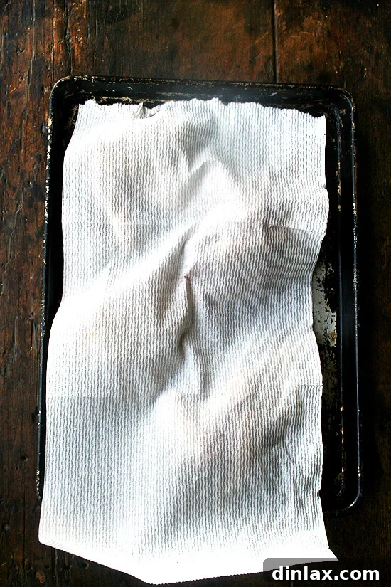 Hands gently patting dry pieces of raw chicken arranged on a sheet pan with paper towels, a critical step for achieving crispy skin and preventing steaming.