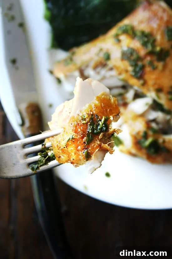 A tantalizing bite of crispy-skinned, herby roasted chicken held by a fork, highlighting the delicious texture and rich flavor in a single mouthful.