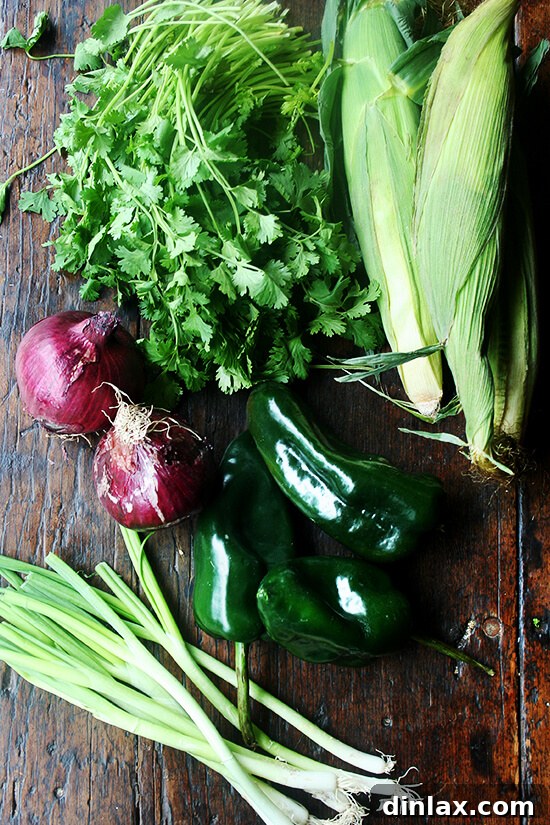 Smoky Grilled Poblano and Corn Salsa Tacos 2 Fresh ingredients laid out for making grilled poblano corn salsa, including poblano peppers, red onions, corn, scallions, limes, and cilantro, ready for preparation.
