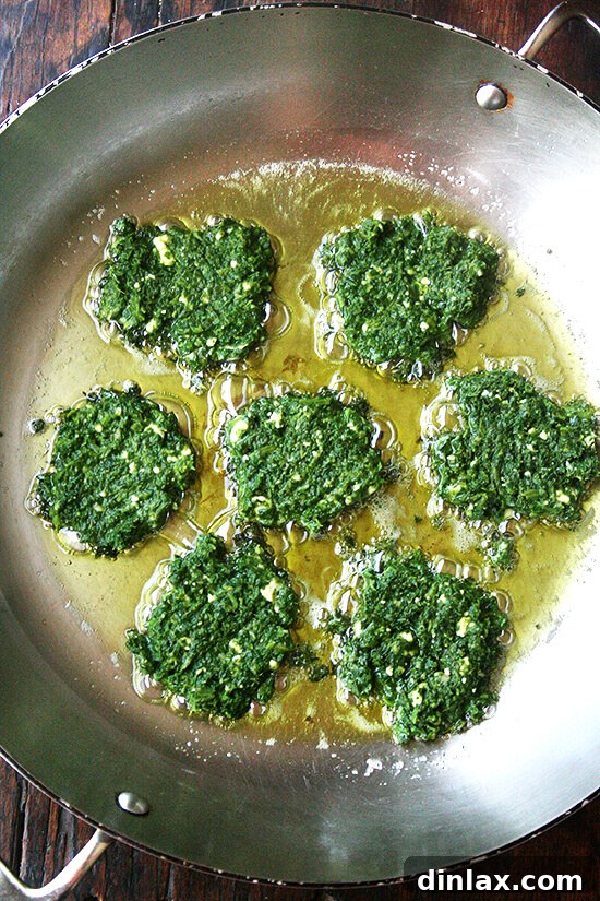 Green fritters sizzling in a frying pan, turning golden brown and crispy.