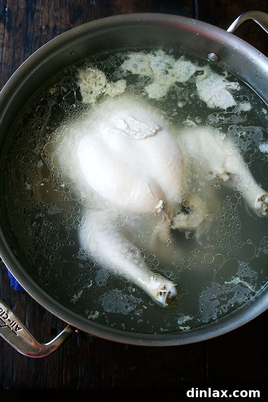 Poached chicken cooling in its cooking liquid, ensuring maximum moisture and tenderness.