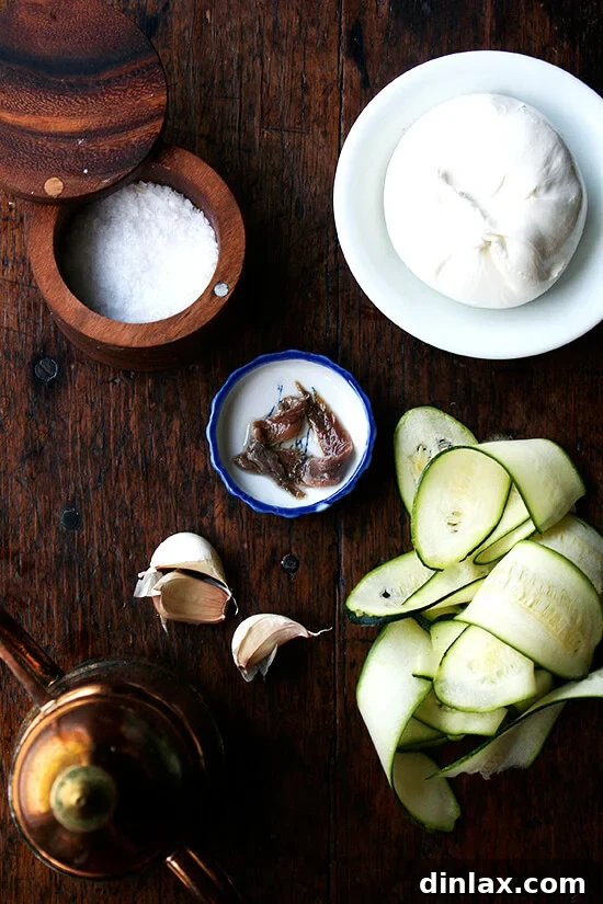 Burrata Basil Summer Squash Pizza 2 A beautifully arranged table of fresh ingredients for the Zucchini Anchovy pizza, featuring glistening anchovies, coarse sea salt, thinly sliced zucchini, aromatic garlic, creamy burrata, and a bottle of rich olive oil.