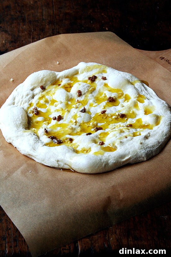 Burrata Basil Summer Squash Pizza 5 A round of pizza dough generously drizzled with olive oil, delicately topped with minced garlic and anchovy, creating a fragrant base for the pizza.