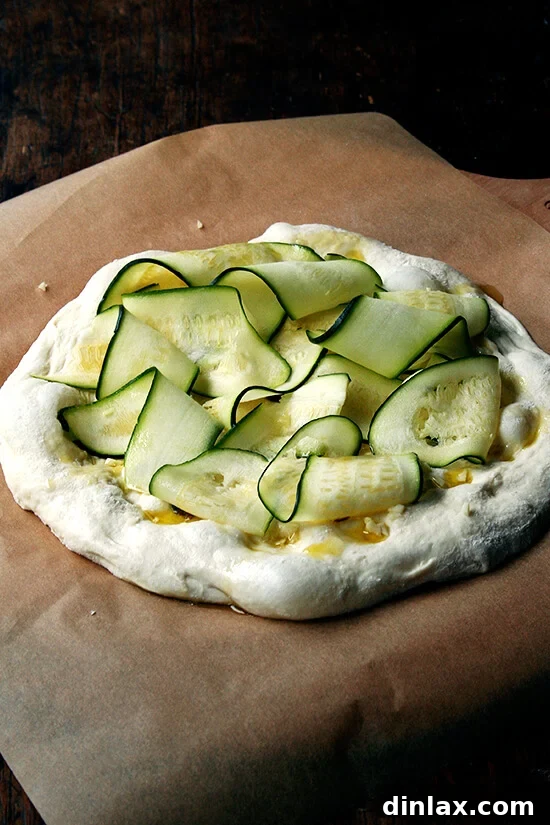 Burrata Basil Summer Squash Pizza 6 A pristine pizza dough round, beautifully adorned with layers of thinly shaved zucchini ribbons, creating an elegant and fresh topping.