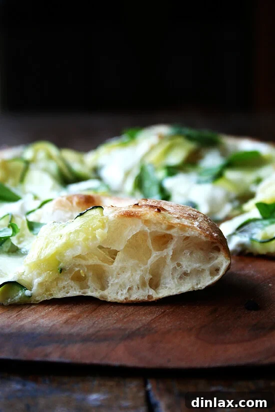 Burrata Basil Summer Squash Pizza 9 A close-up side view of a slice of the baked Zucchini-Anchovy pizza, showcasing its perfectly airy crust, melted cheese, and tender toppings.