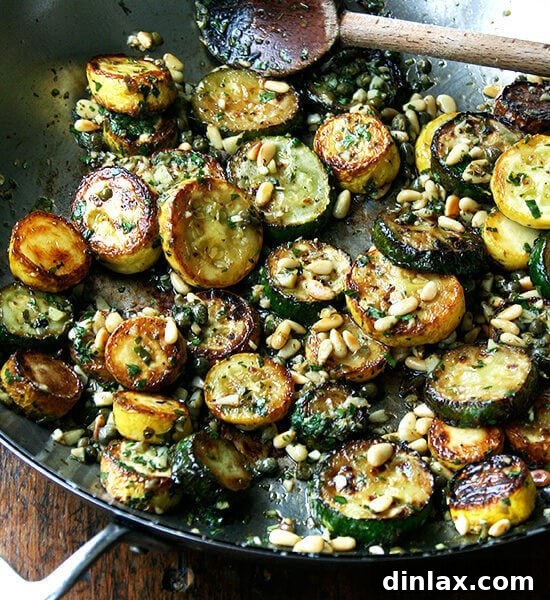 A plate of golden-brown sautéed zucchini with fresh mint, basil, and pine nuts, ready to be served.