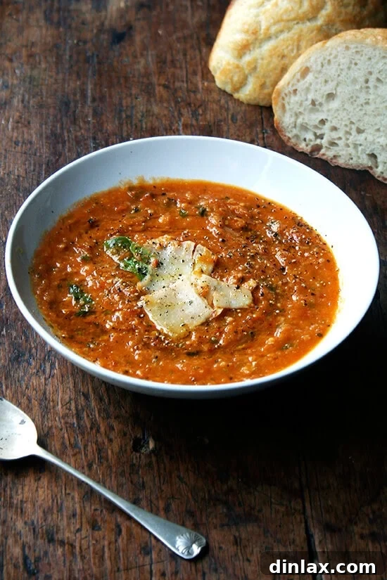 A vibrant bowl of roasted tomato and bread soup, known as Pappa al Pomodoro, served alongside freshly baked bread. A spoon rests in the inviting soup, highlighting its rustic texture and warmth.