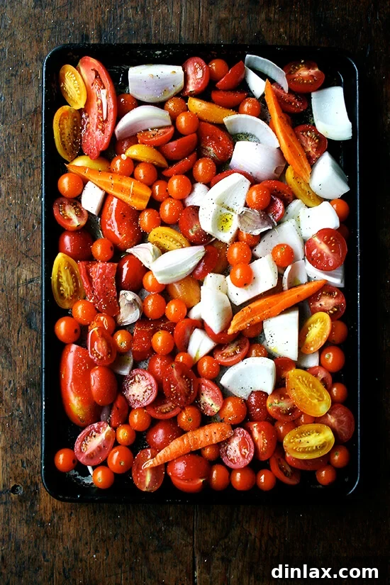 A sheet pan generously loaded with freshly chopped tomatoes, onions, carrots, and garlic, prepped and ready for roasting.