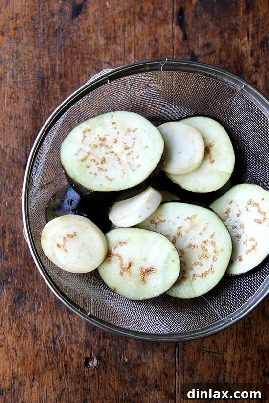 salted eggplant slices draining in a colander, showing beads of moisture