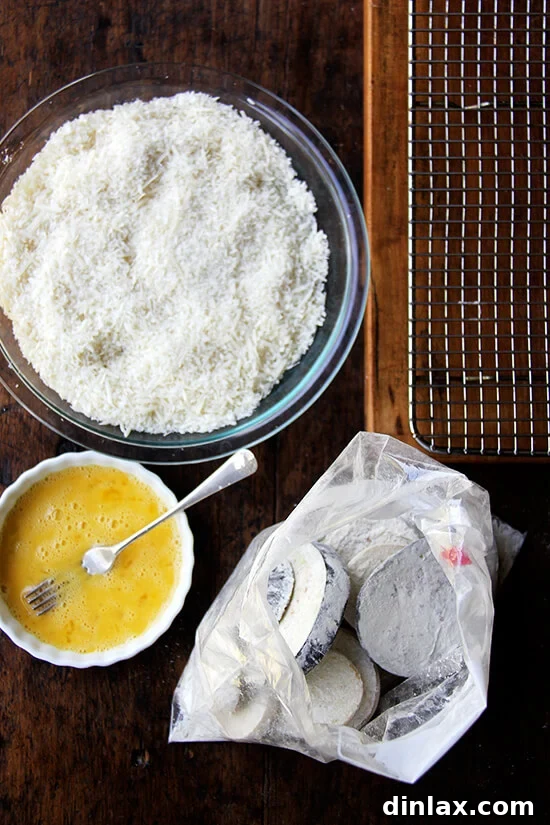 A breading station set up on a table: a bowl of bread crumbs, a bowl of beaten eggs, and eggplant tossed with flour