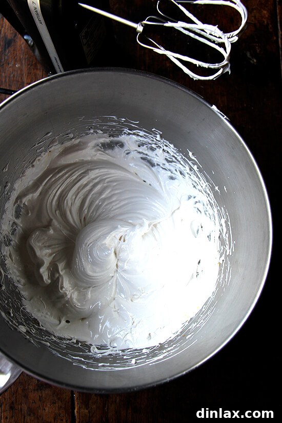 Egg whites, sugar, cream of tartar, and salt being vigorously whipped over a double boiler, transforming into a frothy meringue.